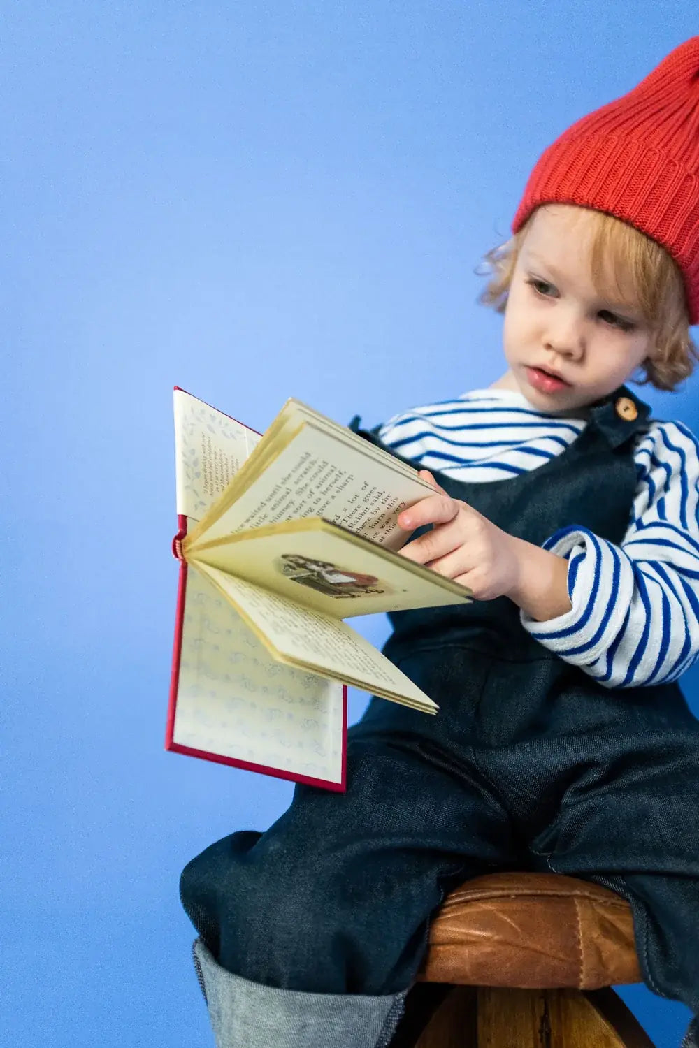 A child in a hat reads an illustrated book.