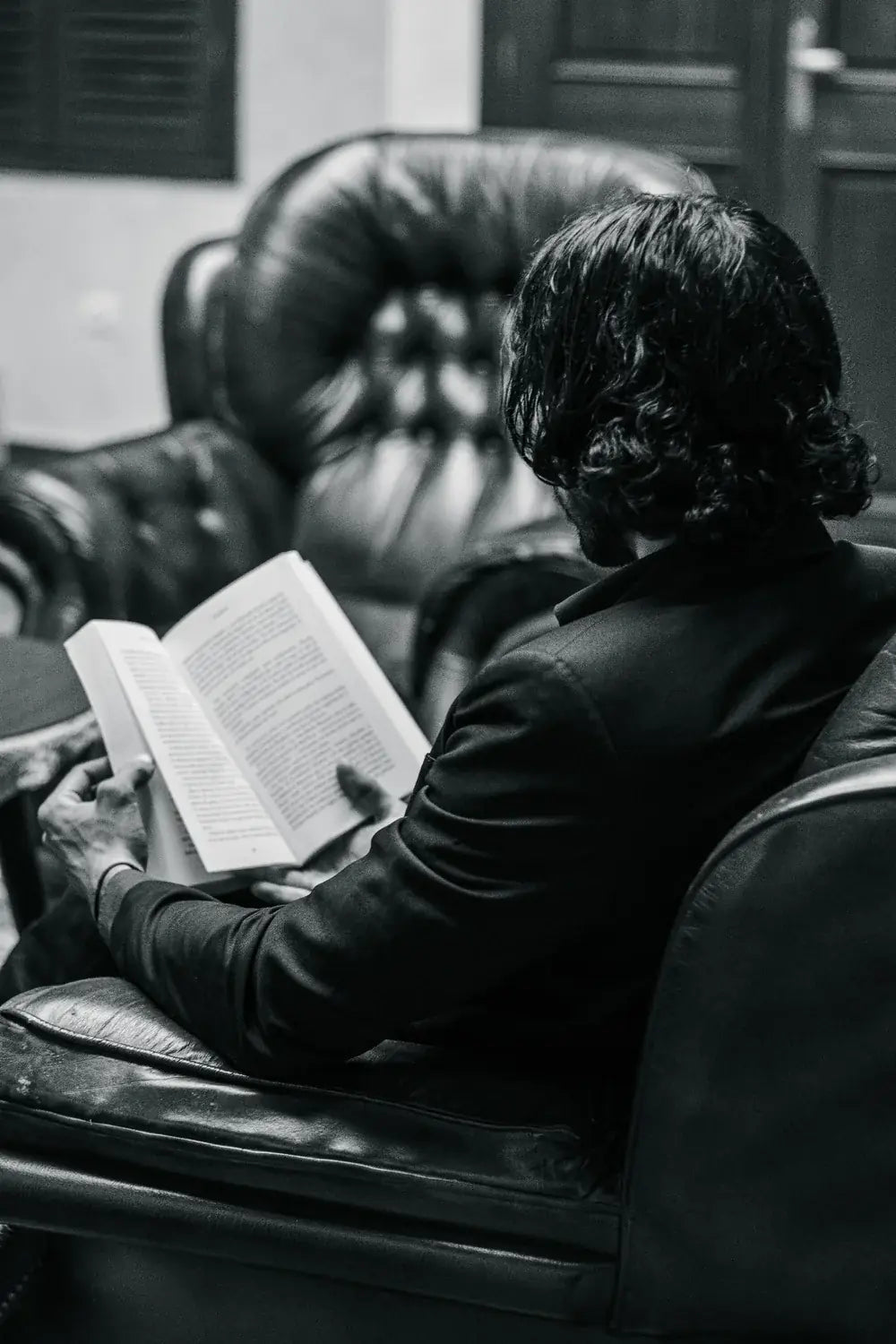 A reader settles into a leather armchair with a book.